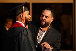A Black CSU staff member helps a Black student with his graduation regalia
